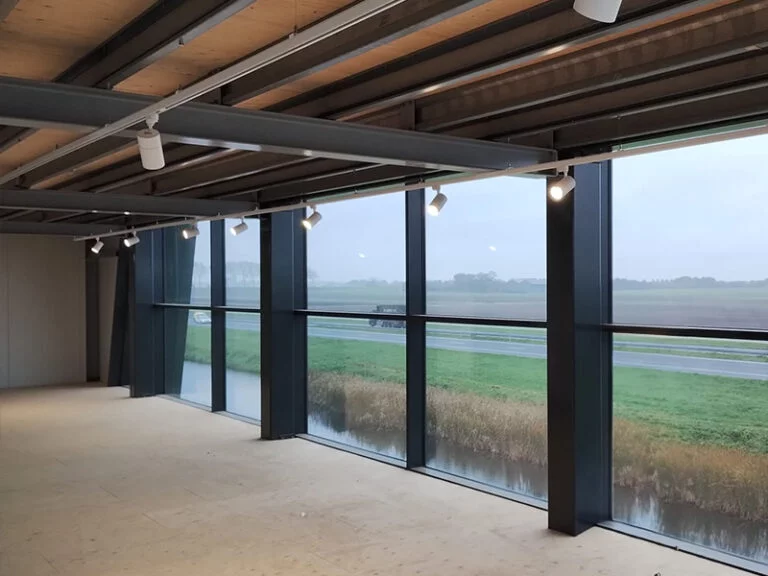 Een modern kantoorinterieur met grote glazen ramen die uitkijken op een mistig landelijk landschap, met zichtbare balken aan het plafond en lineaire verlichting.